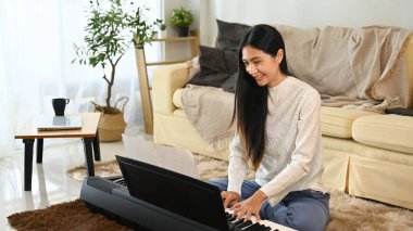 Gülümseyen genç kadın oturma odasında elektrikli piyano çalışıyor..