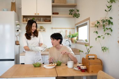 Güzel Asyalı eş, kocasına taze pişmiş yemek ve gülümsemeyle servis ediyor...