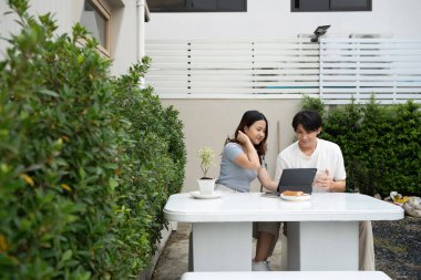 Mutlu genç Asyalı çift dijital tablet kullanıyor ve arka bahçede birlikte vakit geçiriyorlar..