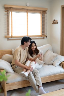 Rahat Asyalı çift oturma odasındaki akıllı telefondan online içeriği izliyor..