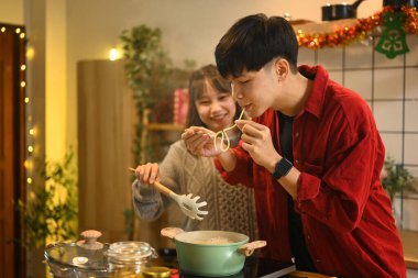 Mutlu genç çift, Noel süsleriyle süslenmiş mutfakta birlikte yemek pişiriyor..