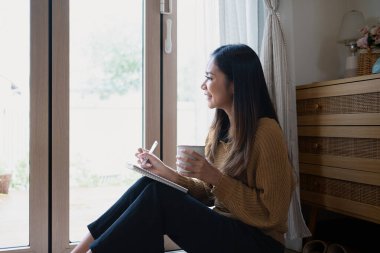 Pencereden dışarı bakarken deftere yazan güzel genç bir kadın..