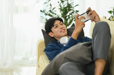 Kulaklıklı genç adam akıllı telefondan video oyunu oynuyor..
