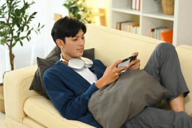 Rahat genç Asyalı adam koltukta oyun oynamanın keyfini çıkarıyor..