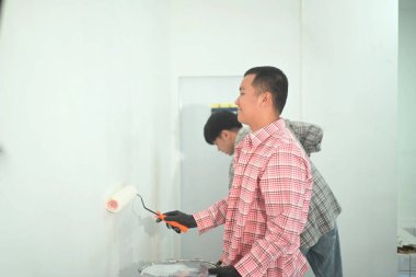 Yenilenmiş alanda boya silindiri kullanarak duvar boyayan genç bir adam. Ev geliştirme kavramı.