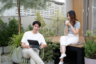 Bahçelerinde sıcak içecek ve dijital tabletle rahatlayan genç bir çift..