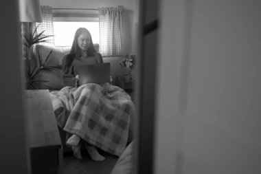 Genç bir kadın kanepeye dizüstü bilgisayar koyup siyah-beyaz bir battaniyeye sarılmış..