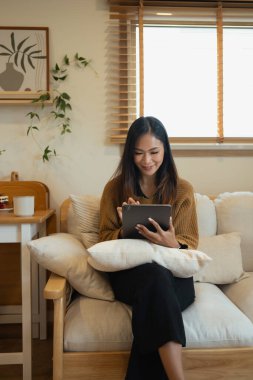 Evdeki dijital tablette süveter giyen güzel genç bir kadın internette geziniyor..