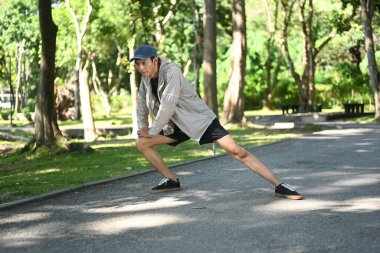 Genç bir adam parkta esniyor, antrenmana ya da koşuya hazırlanıyor. Sağlık ve açık hava faaliyetleri kavramı.