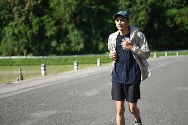 Genç sporcu, güneşli bir günde kaldırımlı bir yolda koşuyor..