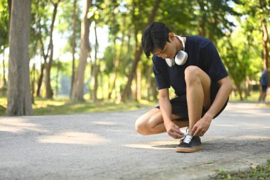 Ayakkabı bağcıklarını bağlamak için parkta çömelmiş koşuya hazırlanan genç adam..