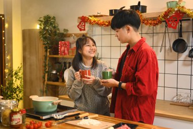 Mutlu genç çift, Noel süsleriyle süslenmiş mutfakta sıcak içeceklerin tadını çıkarıyor..