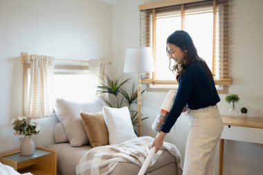 Oturma odasında kablosuz süpürge kullanan neşeli genç bir kadın..
