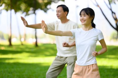 Güzel bir kadın ve orta yaşlı bir adam birlikte parkta Tai Chi yapıyorlar. Farkındalık ve sağlık kavramı.