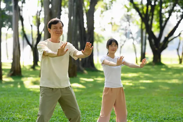 Yaşlı adam ve genç kadın huzur parkında Tai Chi çalışıyor. Farkındalık ve refah kavramı.