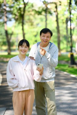 Mutlu orta yaşlı baba ve yetişkin kızı manzaralı bir parkta egzersiz yaptıktan sonra mola veriyorlar..