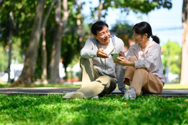 Huzurlu bir parkta antrenmandan sonra gülümseyen orta yaşlı baba ve kızı cep telefonu kullanıyor..