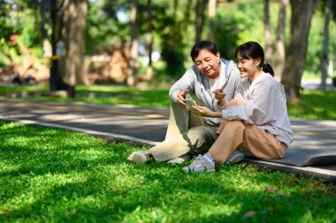 Neşeli kıdemli baba ve kızı parkta asfalt yolda oturuyorlar ve antremandan sonra cep telefonu kullanıyorlar..