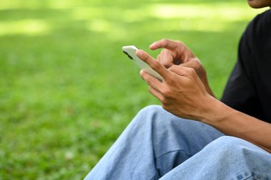 Çimlerin üzerinde cep telefonu kullanan bir adam dışarıda dinlenirken mola veriyor..