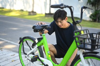 Genç Asyalı bir adam parka gitmeden önce bisiklet teftişi yapıyor..