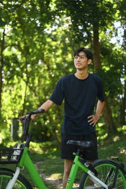 Yakışıklı Asyalı adam bisikletinin yanında duruyor ve güzel parkta Miles 'a bakıyor..