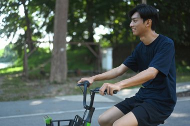 Mutlu Asyalı adam bisikletini manzaralı yolda sürüyor. Açık havada egzersizin tadını çıkarıyor..