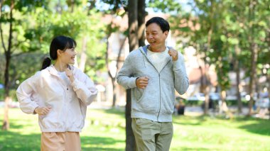 Mutlu kıdemli adam ve kızı ağaçların arasında koşuyorlar ve sabah sporlarının tadını çıkarıyorlar..