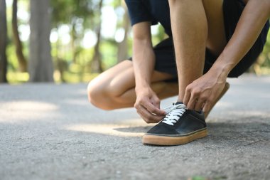 Ayakkabı bağcıklarını bağlayan genç sporcuyu yeşil bir parkta koşuya hazırlayın..