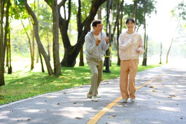 Mutlu yaşlı bir adam ve kızı egzersiz rutininden zevk alıyorlar, birlikte parkta koşuyorlar..