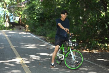 Mutlu genç adam ağaçların arasından geçen güneşli bir yolda bisiklet sürüyor..