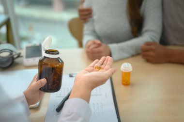 Doktor elinde bir şişe hap tutuyor ve hastaya tedavi planını anlatıyor..