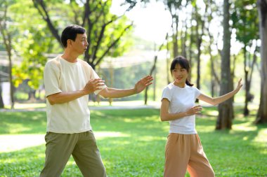 Orta yaşlı baba ve kızı huzur parkında Tai Chi çalışıyor. Aile aktiviteleri, sağlık ve refah kavramı.