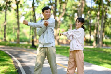 Mutlu yetişkin kız ve babası sabah sporu için sakin bir parkta ısınıyorlar..