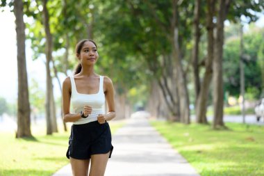 Genç bir kadın, güzel bir parkta yol boyunca ferahlatıcı koşudan hoşlanır..