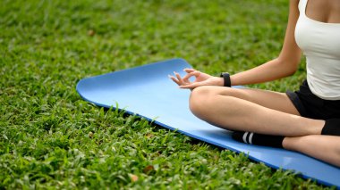 Yeşil parktaki yoga minderinde dizlerinin üstüne çökmüş, elini meditasyon jestine sokmuş, sakin bir kadın..