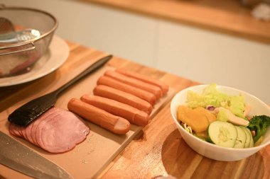 Dilimlenmiş jambon, sosis ve bir kase salata ile ahşap mutfak tezgahını kapat..
