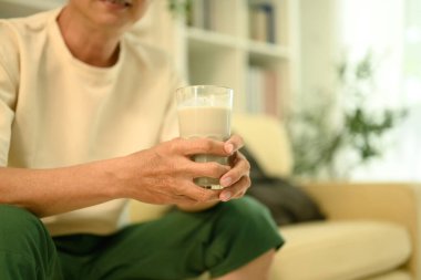 Kanepede oturan, elinde bir bardak süt tutan orta yaşlı bir adam. Sağlık ve beslenme kavramı.