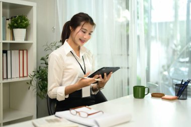 Gülümseyen genç girişimci çalışma alanındaki dijital tabletinin notlarını inceliyor.