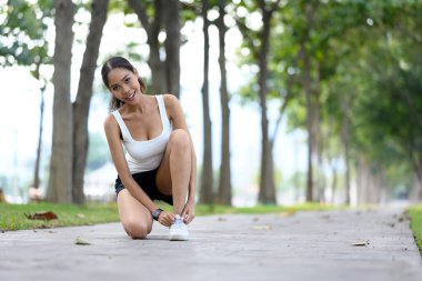 Çekici genç bir kadın, ayakkabı bağcıklarını patikada bağlayıp parkta koşuya hazırlanıyor..