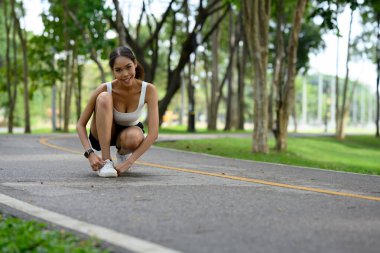 Neşeli genç bir kadın parkta spor ayakkabılarını düzeltiyor..