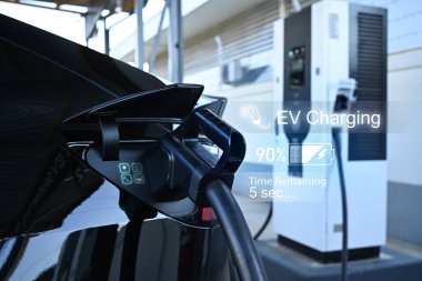 Şarj istasyonuna takılı bir elektrikli araba, akü ilerlemesi ile dijital arayüzü görüntülüyor.