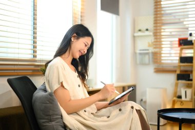 Neşeli genç kadın serbest çizim yapıyor ya da dijital tabletine not alıyor..