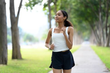 Güneşli bir günde ağaçların arasında koşan genç bir kadın..