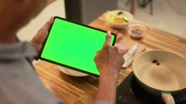 Bir yemek tarifini ya da yemek talimatlarını takip etmek için rahat bir mutfakta dijital tablet kullanan kıdemli adamı kapat..