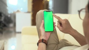 Evdeki kanepede uzanırken elinde yeşil ekran olan akıllı telefonu tutan adama yaklaş..