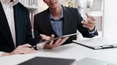 Resmi takım elbiseli iş arkadaşları toplantı sırasında bir tabletteki bilgileri gözden geçiriyorlar.