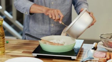 Orta yaşlı bir adam pilav kepçesiyle kızartma tavasına pilav koyuyor ve ev mutfağında lezzetli yemekler pişirmeye hazır..