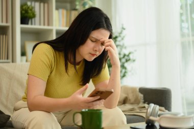 Akıllı telefonu tutan ve kafaya kapalı gözlerle dokunan genç bir kadın, baş ağrısı ya da yorgunluk hissediyor..