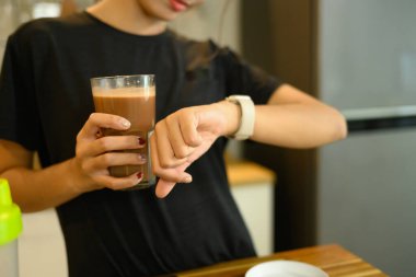 Genç adam bir bardak çikolatalı protein içeceği tutuyor ve onun akıllı hareketlerini kontrol ediyor..