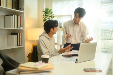 Gülümseyen öğretmen, bir öğrenciye ders sırasında rehberlik eder..